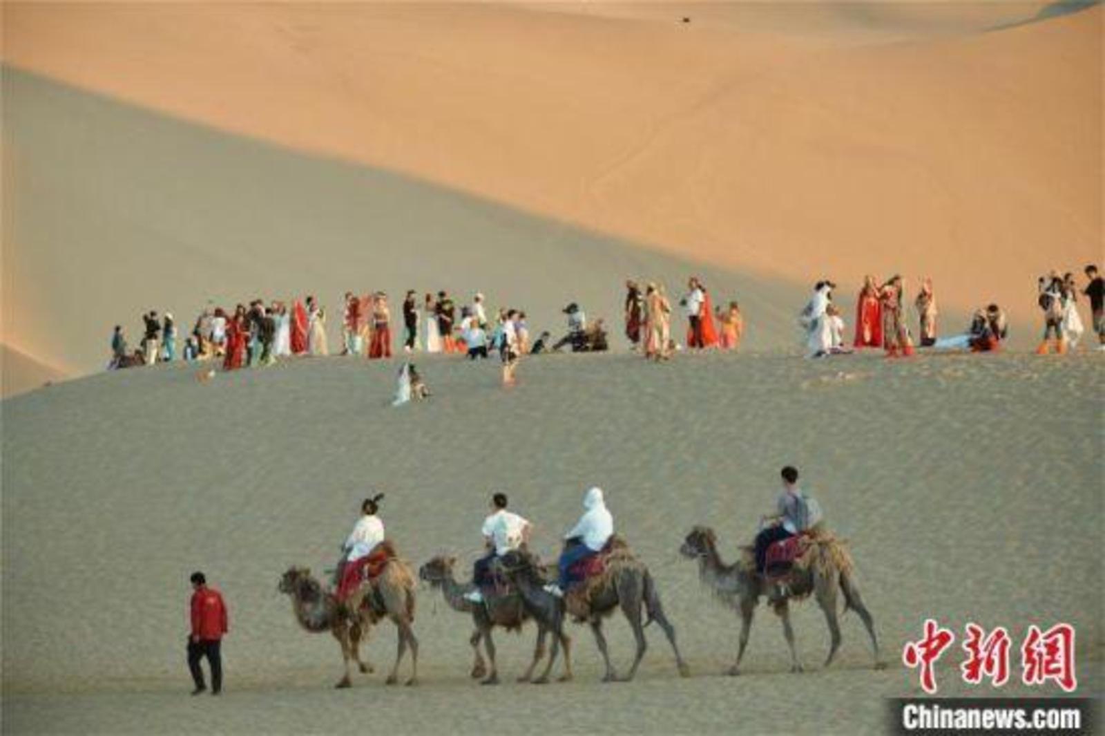 2023年6月7日，游客身着特色服饰和自己的旅拍团队在鸣沙山上拍摄敦煌旅拍纪念照。　王斌银 摄